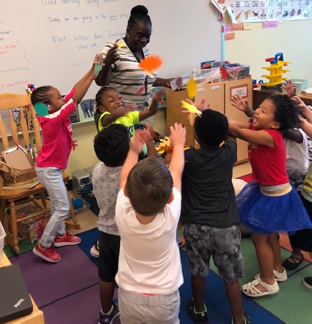 Eight children in a classroom playing with their teacher.
